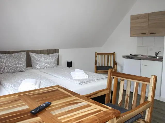 Schlafzimmer mit Holztisch und der Küche im Hintergrund